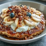 Morning Protein Pancake Bowl topped with a honey drizzle, chopped nuts, and crunchy granola for added texture.