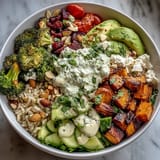 A colorful grain bowl featuring quinoa, baked tofu, avocado, cherry tomatoes, and crunchy seeds, topped with green goddess dressing.  