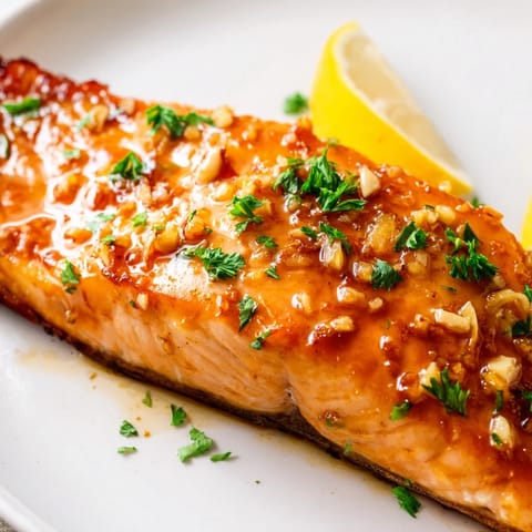 Honey Garlic Glazed Salmon roasted to tender perfection, served with lemon wedges alongside steamed rice and vibrant green veggies.  