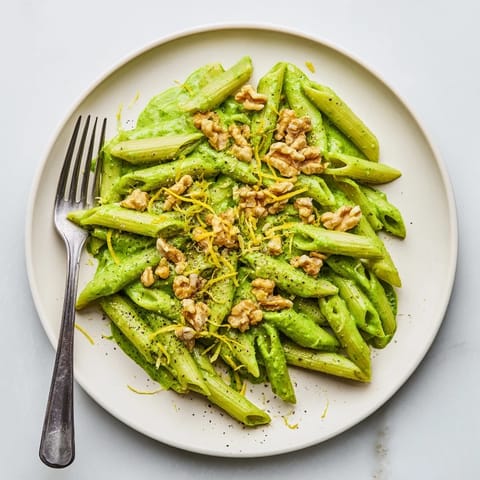 A close-up of vegan Creamy Spinach Walnut Pasta twirled on a fork, revealing the vibrant green, velvety sauce coating every noodle.  