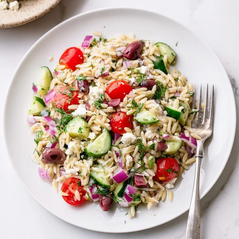 Bright Greek Orzo Salad served in a glass salad bowl, garnished with fresh parsley and lemon slices on a wooden table.  