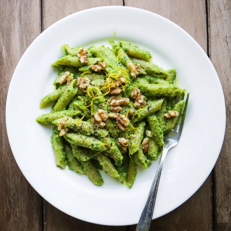 Overhead view of Creamy Spinach Walnut Pasta on a rustic table, garnished with fresh spinach leaves and freshly ground black pepper.