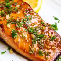 Four golden-brown Honey Garlic Glazed Salmon fillets rest on a baking sheet, glistening with sticky sauce and garnished with fresh parsley.  